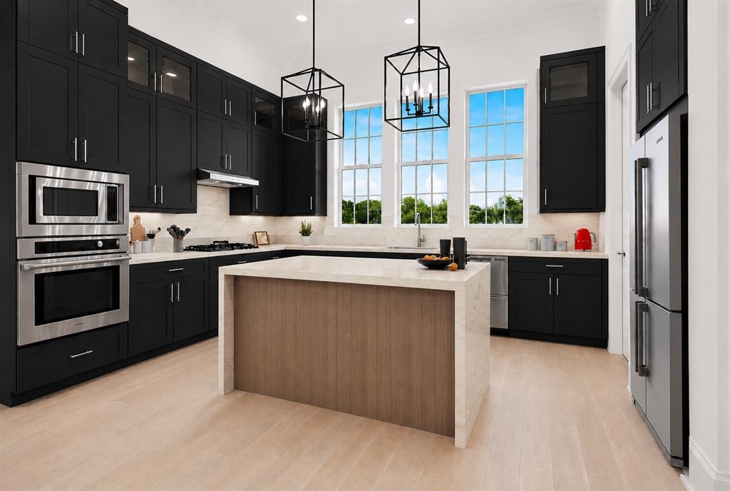 Gourmet kitchen featuring dark cabinetry, stainless steel appliances, a center island with a light-toned countertop, and multiple large windows Gourmet kitchen featuring dark cabinetry, stainless steel appliances, a center island with a light-toned countertop, and multiple large windows