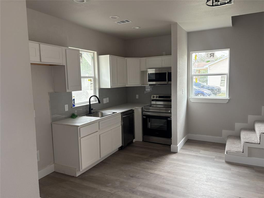 Modern kitchen featuring white cabinetry, light gray countertops, stainless steel appliances, a black gooseneck faucet, and wood-finish flooring