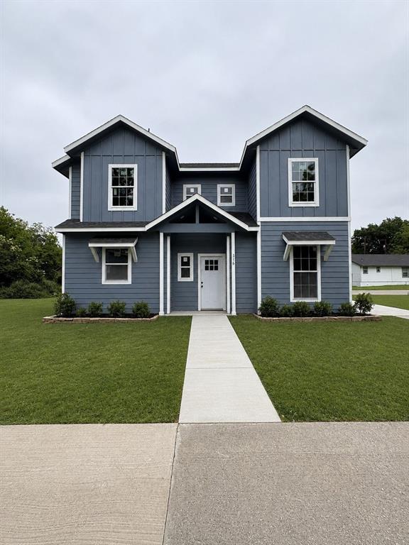 Two-story residence featuring a blue board and batten facade with white trim, a covered entry porch, multiple window awnings, and a concrete pathway leading to the front door