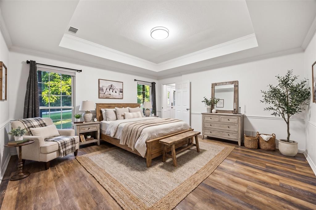 Spacious bedroom featuring wood-finish flooring, tray ceiling, and crown molding