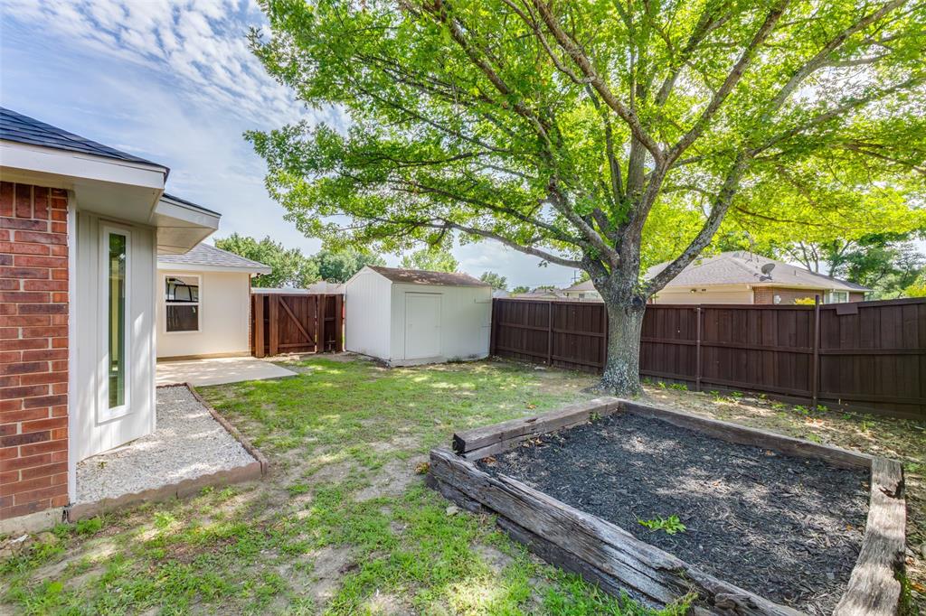 Spacious backyard featuring a substantial tree providing natural shade, a raised garden bed, a white storage shed, and a privacy fence