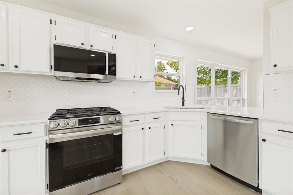 Modern kitchen featuring white cabinetry, stainless steel appliances, a white herringbone tile backsplash, light wood-finish flooring, and white countertops