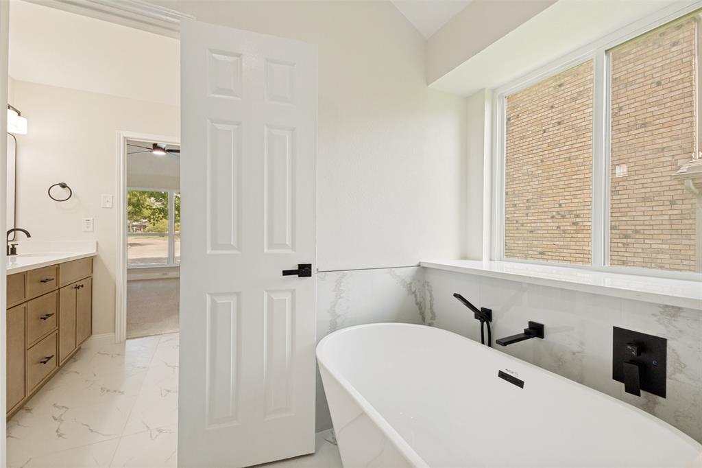 Freestanding soaking tub with matte black fixtures, set against a tiled accent wall and large windows