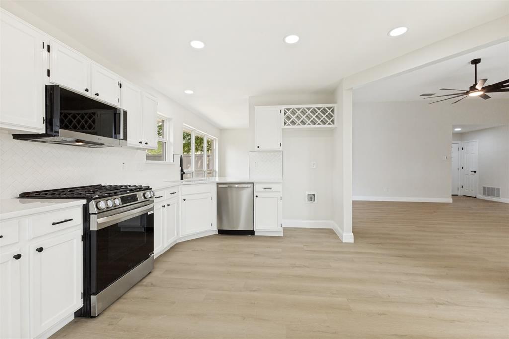 Bright kitchen featuring white cabinetry, stainless steel appliances, light-toned wood-finish flooring, recessed lighting, and an integrated wine rack