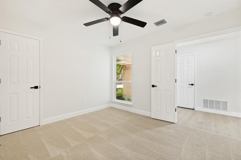 Spacious room featuring neutral paint, light-colored carpet, a ceiling fan with integrated lighting, a large window, and multiple panel doors with matte black hardware