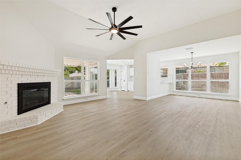 Open concept living area featuring wood-finish flooring, a white brick fireplace, vaulted ceilings, and a modern ceiling fan Open concept living area featuring wood-finish flooring, a white brick fireplace, vaulted ceilings, and a modern ceiling fan