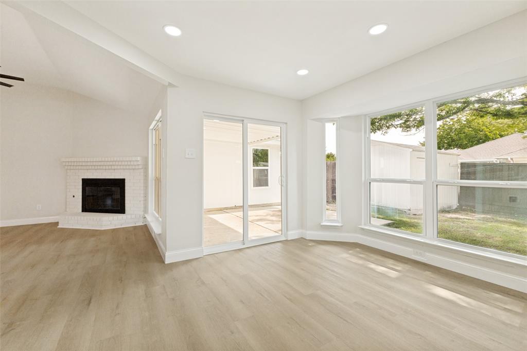 Spacious interior featuring light wood-finish flooring, recessed lighting, and a white brick fireplace Spacious interior featuring light wood-finish flooring, recessed lighting, and a white brick fireplace