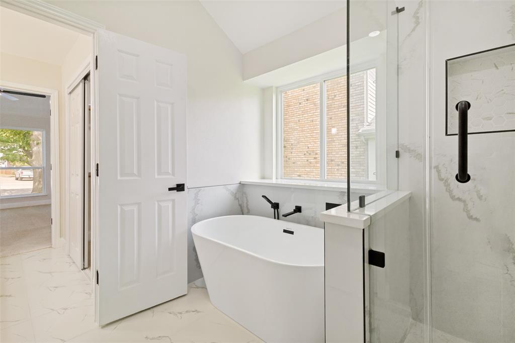 Bathroom featuring a freestanding tub with a wall-mounted faucet, a glass-enclosed shower, and white tile flooring