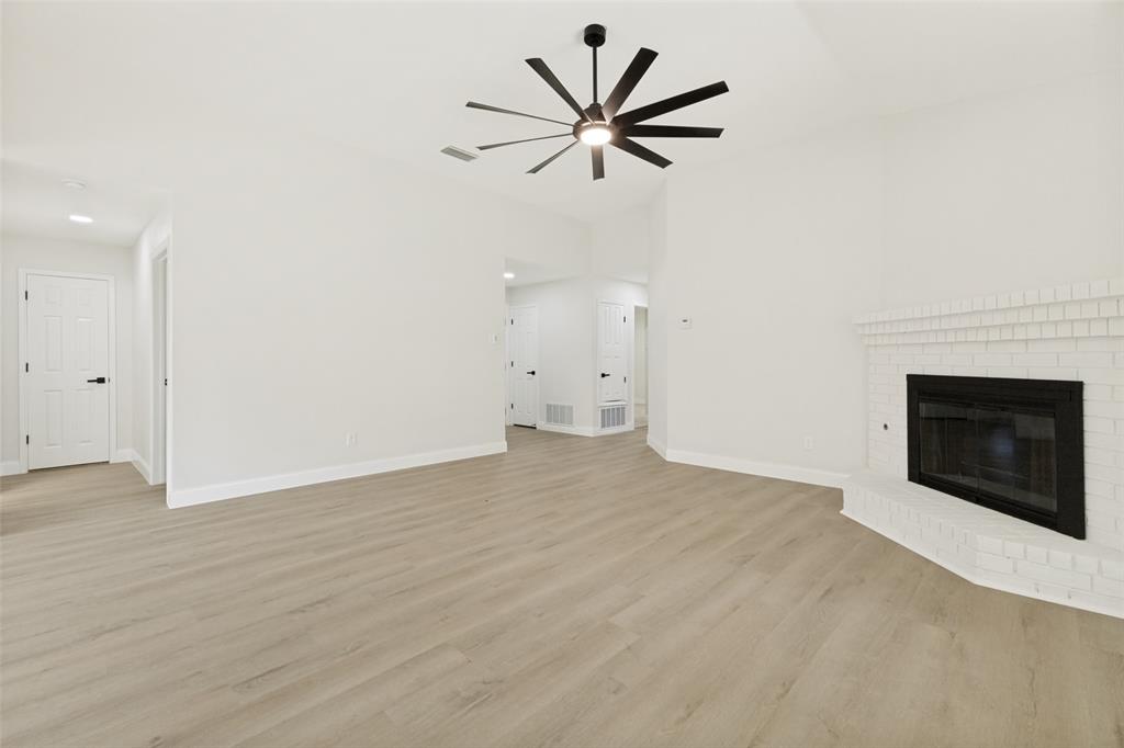 Spacious room featuring vaulted ceilings, wood-finish flooring, a modern ceiling fan with integrated lighting, and a white brick fireplace Spacious room featuring vaulted ceilings, wood-finish flooring, a modern ceiling fan with integrated lighting, and a white brick fireplace