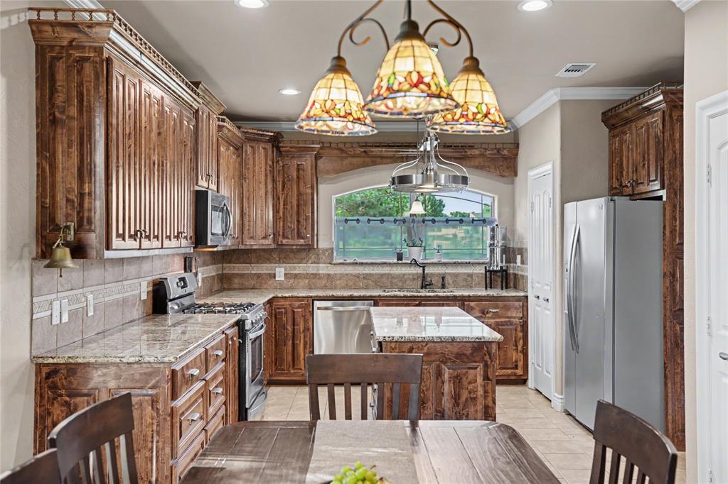 Kitchen featuring extensive wood cabinetry with crown molding, granite countertops, an undermount sink, stainless steel appliances, and tile flooring