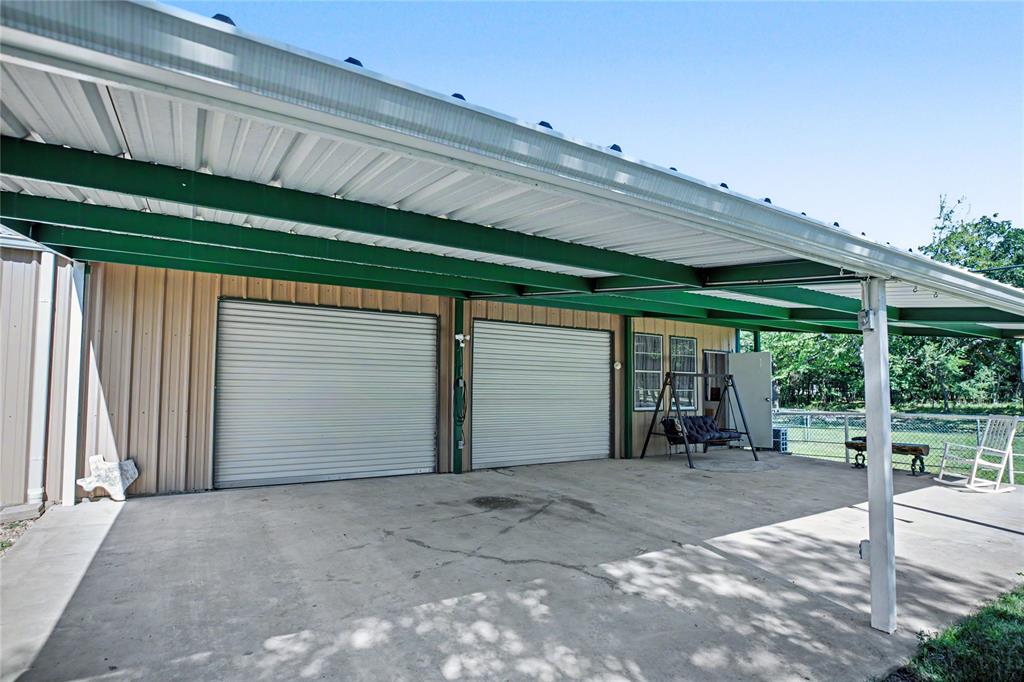 Two garage bays with roll-up doors, extended concrete pad, and a covered patio area with a metal roof