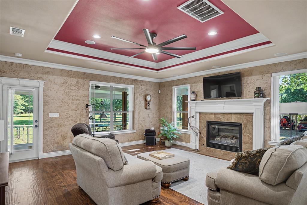 Living area featuring wood-finish flooring, a tray ceiling with recessed lighting and a ceiling fan, and multiple windows