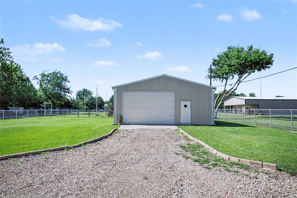 Metal outbuilding featuring a large roll-up door, pedestrian entry, and a gravel driveway with brick edging