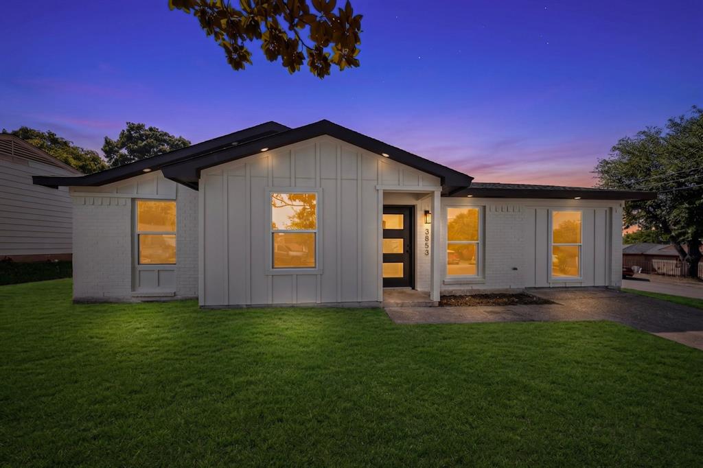 Contemporary-style home featuring a dark shingle roof, white vertical siding, and a contrasting dark entry door with horizontal glass panels Contemporary-style home featuring a dark shingle roof, white vertical siding, and a contrasting dark entry door with horizontal glass panels