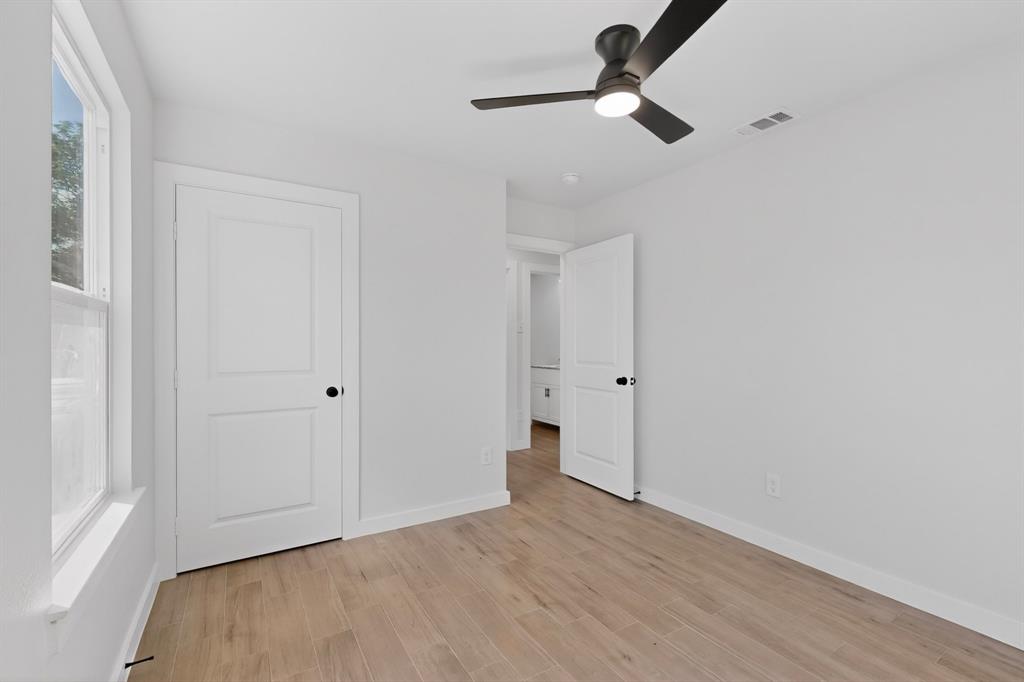 Bright interior room featuring wood-finish flooring, a contemporary ceiling fan with integrated lighting, and a white two-panel door