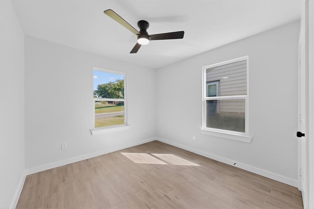 Bright room featuring two windows, light wood-finish flooring, white baseboards, and a contemporary ceiling fan with lighting