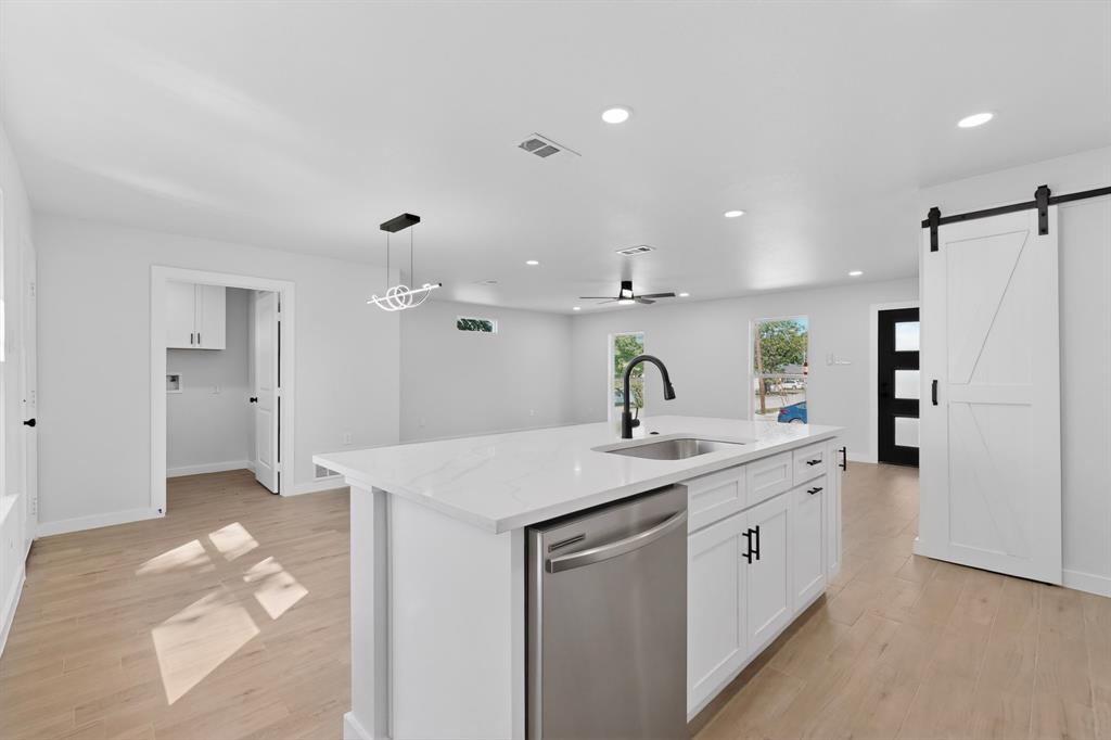 Open-concept kitchen featuring a large island with white cabinetry, stainless steel dishwasher, and a matte black gooseneck faucet