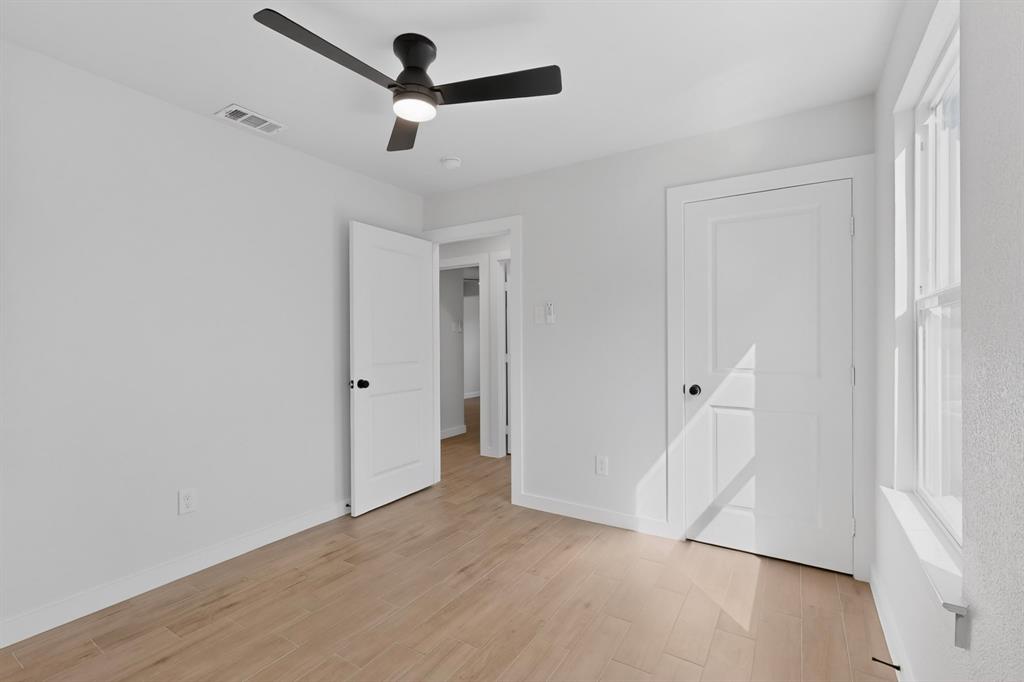 Interior room featuring wood-finish flooring, white walls, and a contemporary black ceiling fan with integrated lighting