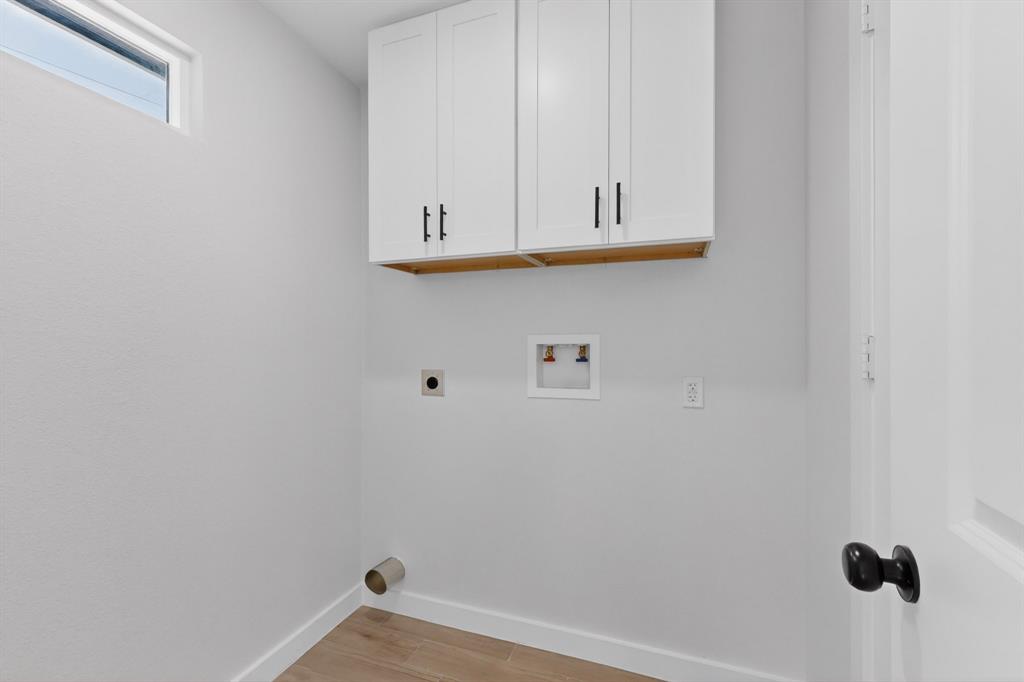 Utility space featuring white shaker-style cabinetry with black hardware, wood-finish flooring, and a high transom window