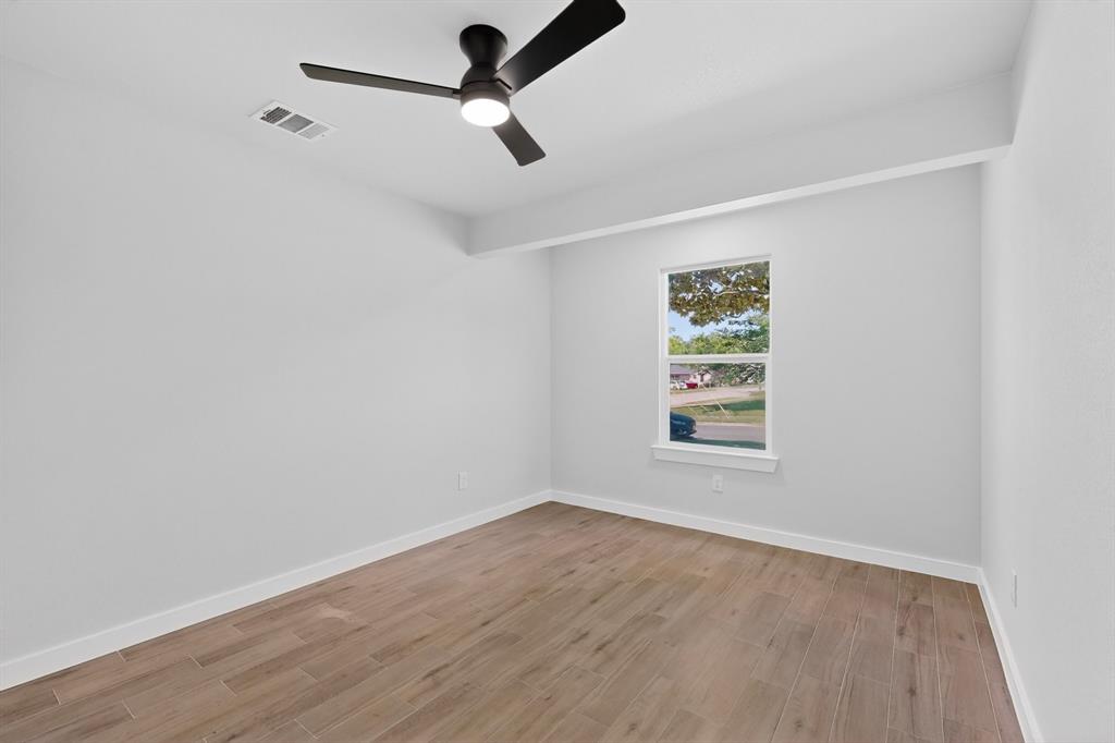 Spacious room featuring wood-finish flooring, a modern black ceiling fan with integrated lighting, a single window, and crisp white walls