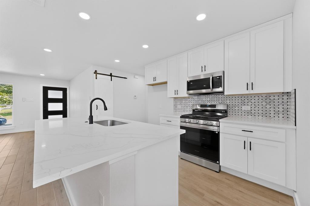 Modern kitchen featuring an expansive island with an undermount sink and matte black faucet, stainless steel appliances, white cabinetry with contrasting hardware, and a graphic tile backsplash