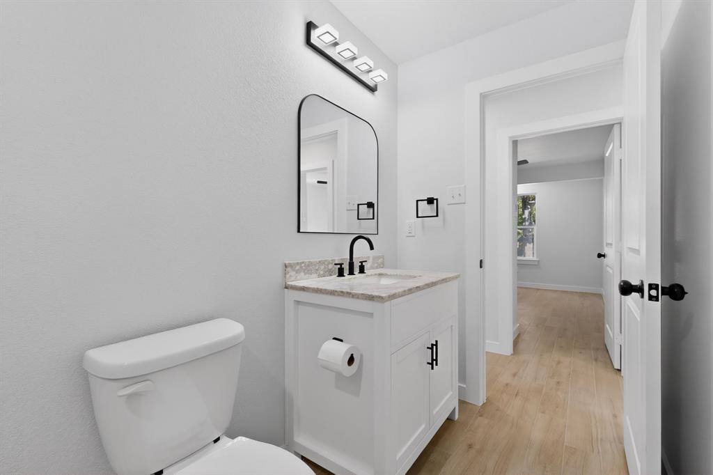 Bathroom featuring a white vanity with a stone-finish countertop, black hardware, an arched mirror, and a modern light fixture