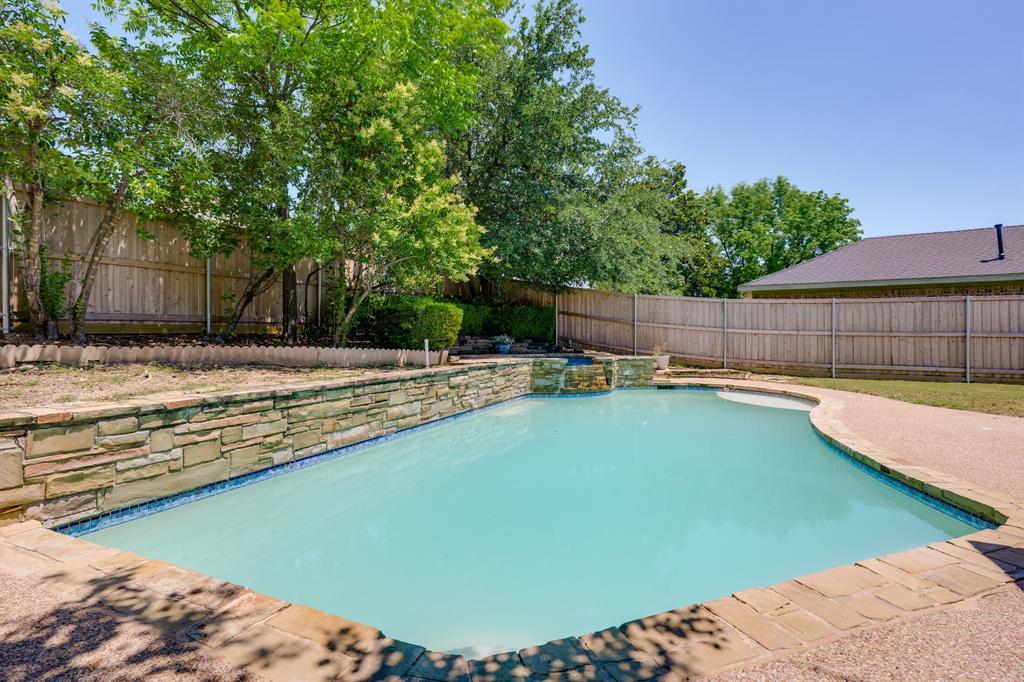 Freeform swimming pool featuring a stone-clad raised spa with waterfall, flagstone coping, and exposed aggregate decking