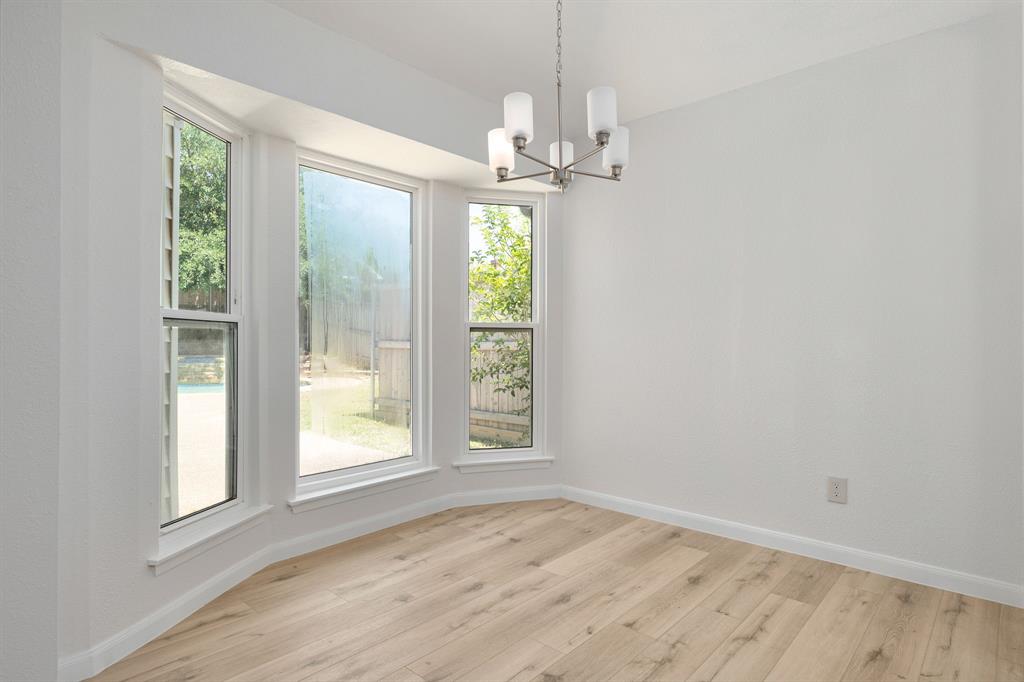 Bay window with white trim, wood-finish flooring, white walls, and a contemporary chandelier