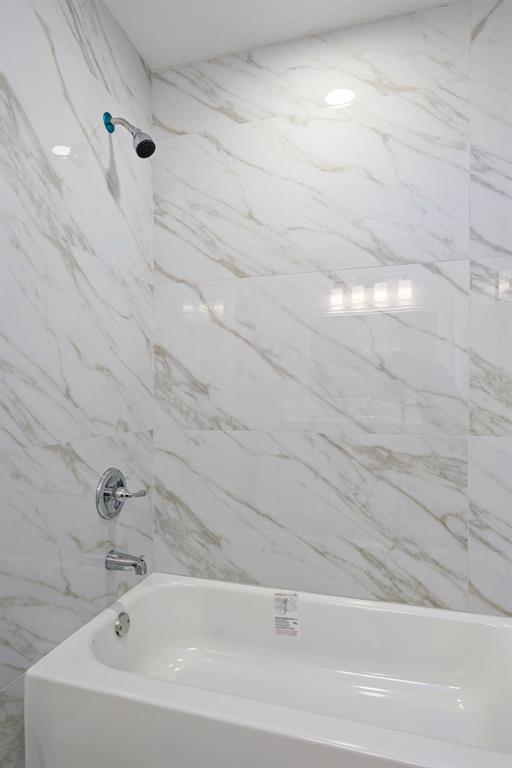 Shower and tub combination featuring white marble-patterned wall tiling and chrome fixtures