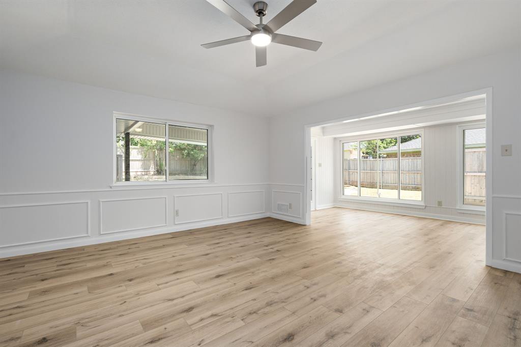 Open living area featuring light wood-finish flooring, white paneling, and a modern ceiling fan