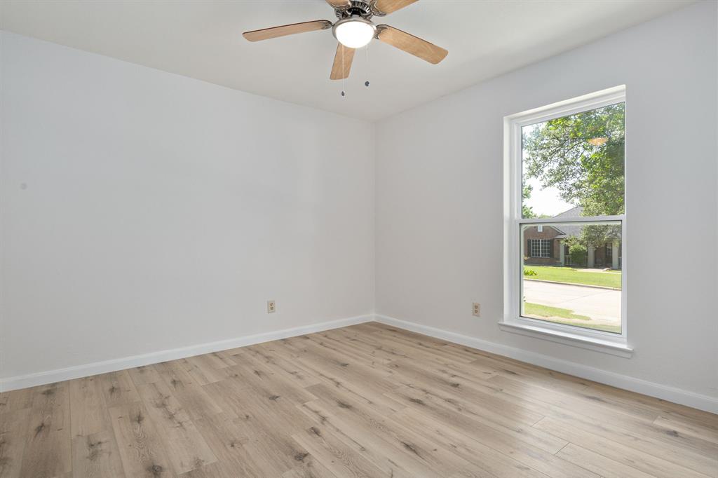 Spacious room featuring wood-finish flooring, crisp white walls, and a large window