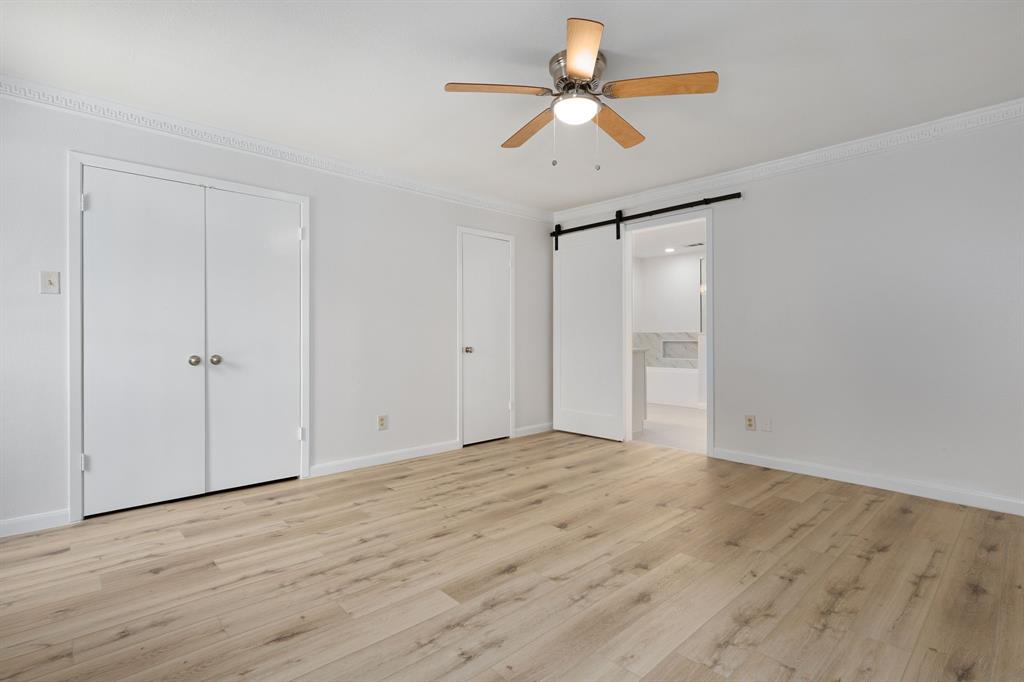 Spacious room featuring wood-finish flooring, ceiling fan with light fixture, crown molding, and a barn door leading to an adjoining area