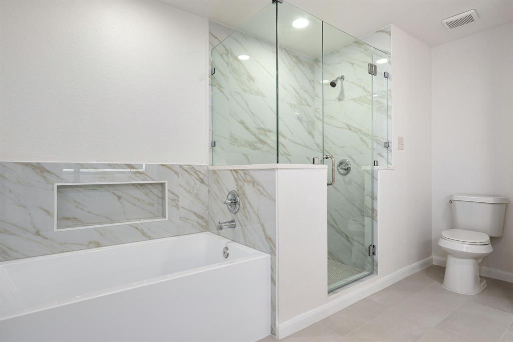 Contemporary bathroom featuring a freestanding tub, glass-enclosed shower, white marble-look wall tiling, recessed shower lighting, and light-toned floor tiling