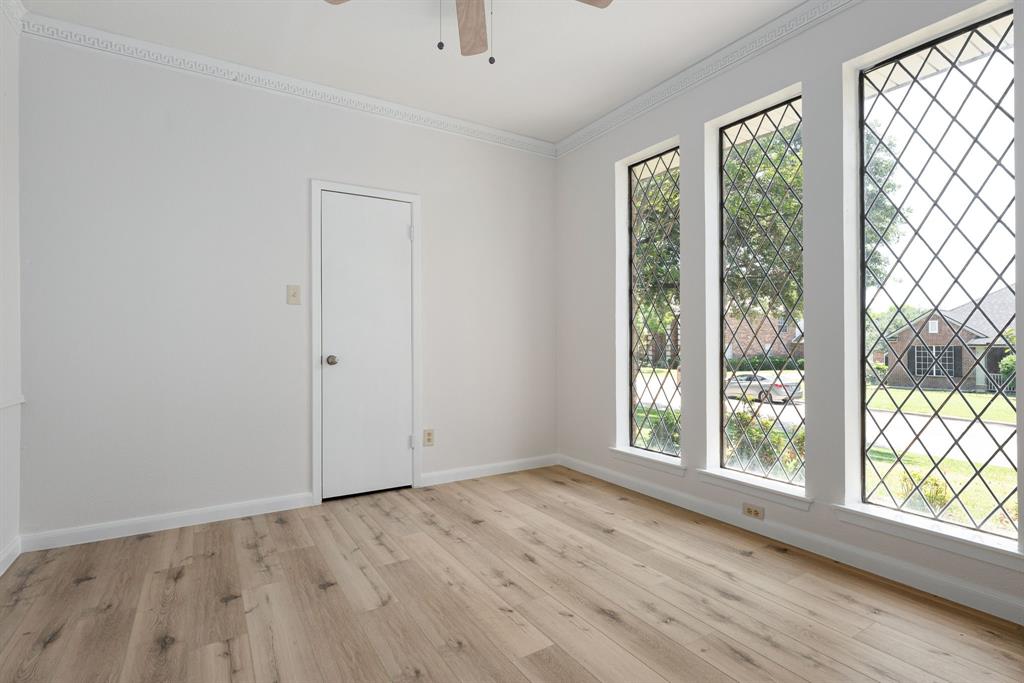 Room featuring three tall windows with diamond-patterned grilles, wood-finish flooring, a white door, and crown molding Room featuring three tall windows with diamond-patterned grilles, wood-finish flooring, a white door, and crown molding