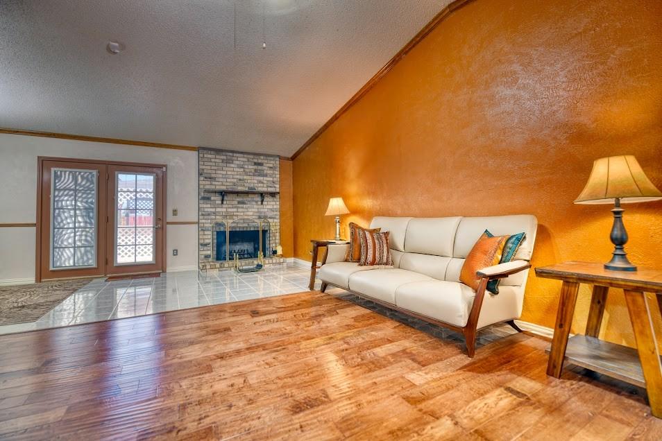 Wood-finish flooring, brick fireplace, vaulted ceiling, and double glass-paneled doors