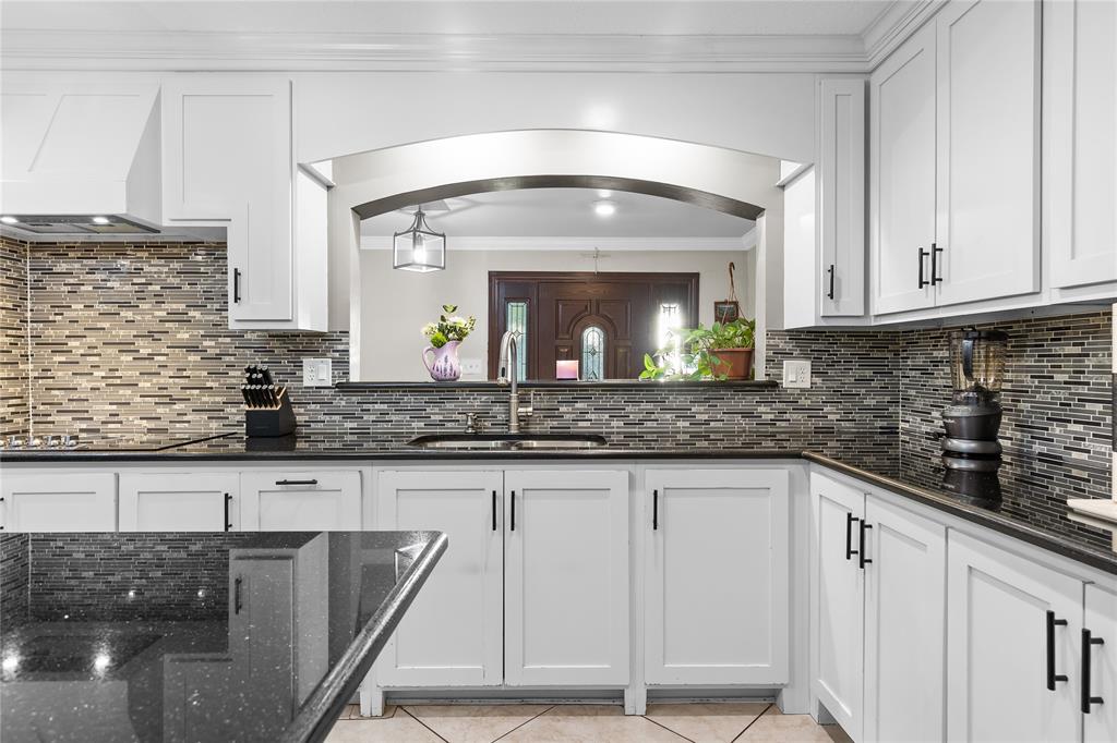 Kitchen featuring white shaker cabinetry with black hardware, dark speckled countertops, and a full-height mosaic tile backsplash