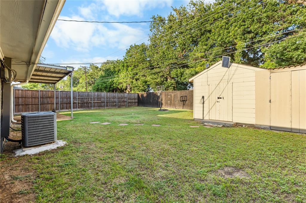 Spacious backyard featuring a manicured lawn, full privacy fencing, a covered patio area, and a detached storage shed