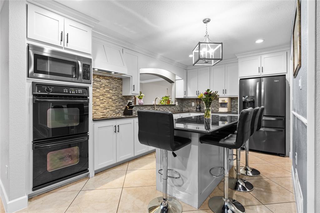 Kitchen featuring white cabinetry, a built-in microwave, double wall ovens, a dark-finish refrigerator, and a kitchen island with dark countertops
