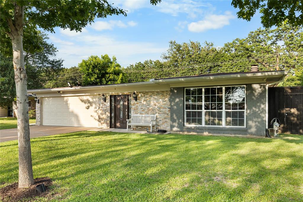 Exterior featuring a split-face stone facade, painted brick accents, an attached two-car garage, multi-pane windows, and a dark wood entry door with glass inserts