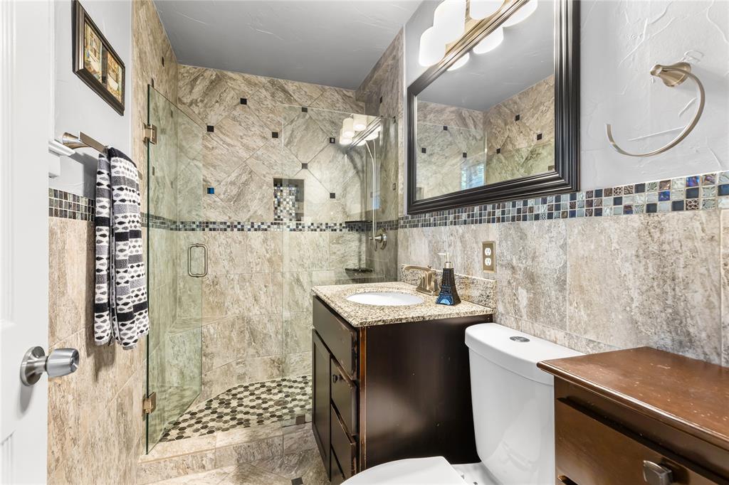 Glass-enclosed shower with stone tile surround and mosaic floor