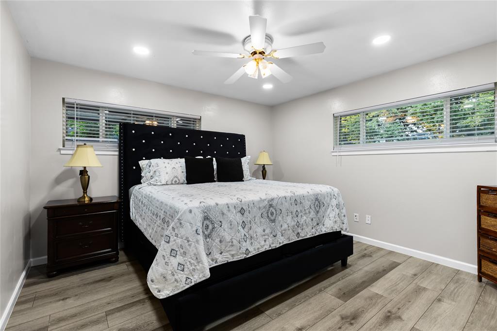 Spacious room featuring wood-finish flooring, two large windows with blinds, recessed lighting, and a ceiling fan with integrated lighting