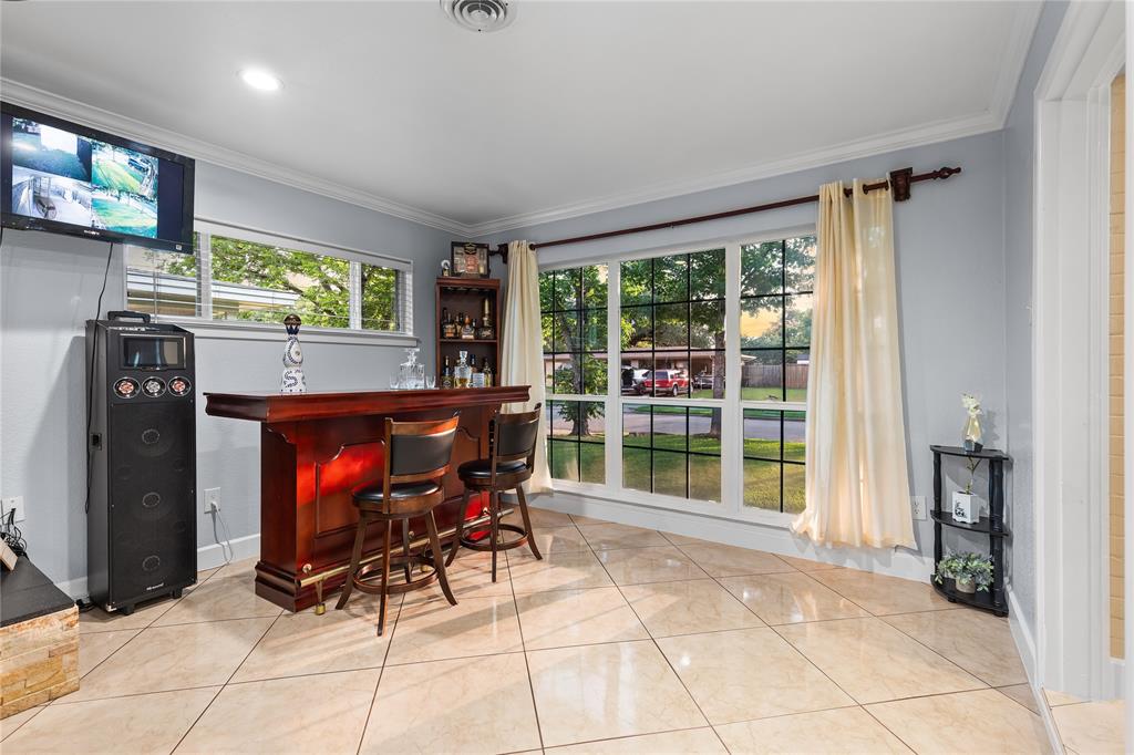 Spacious room featuring a rich wood-finish bar with brass accents, large windows providing ample natural light, recessed lighting, and tile flooring