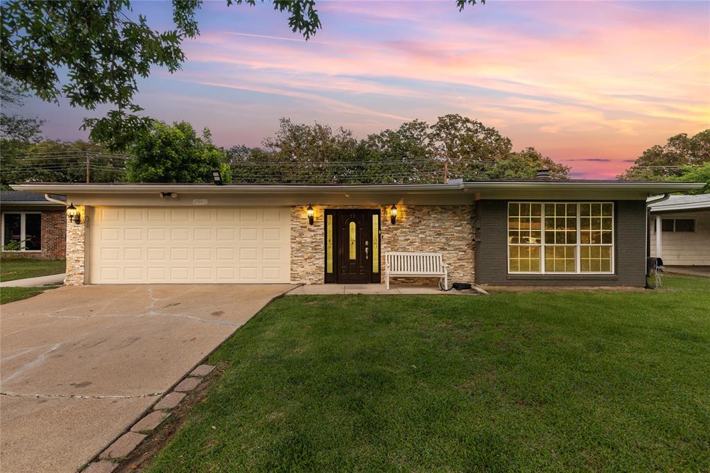 Mid-century ranch-style exterior featuring a two-car garage, stone veneer accents, a dark wood entry door, and a large multi-pane window Mid-century ranch-style exterior featuring a two-car garage, stone veneer accents, a dark wood entry door, and a large multi-pane window