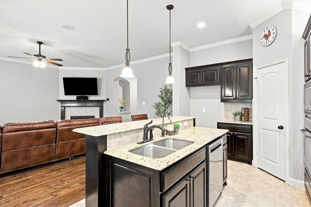 Kitchen island with a double basin stainless steel sink, granite countertops, and dark wood cabinetry