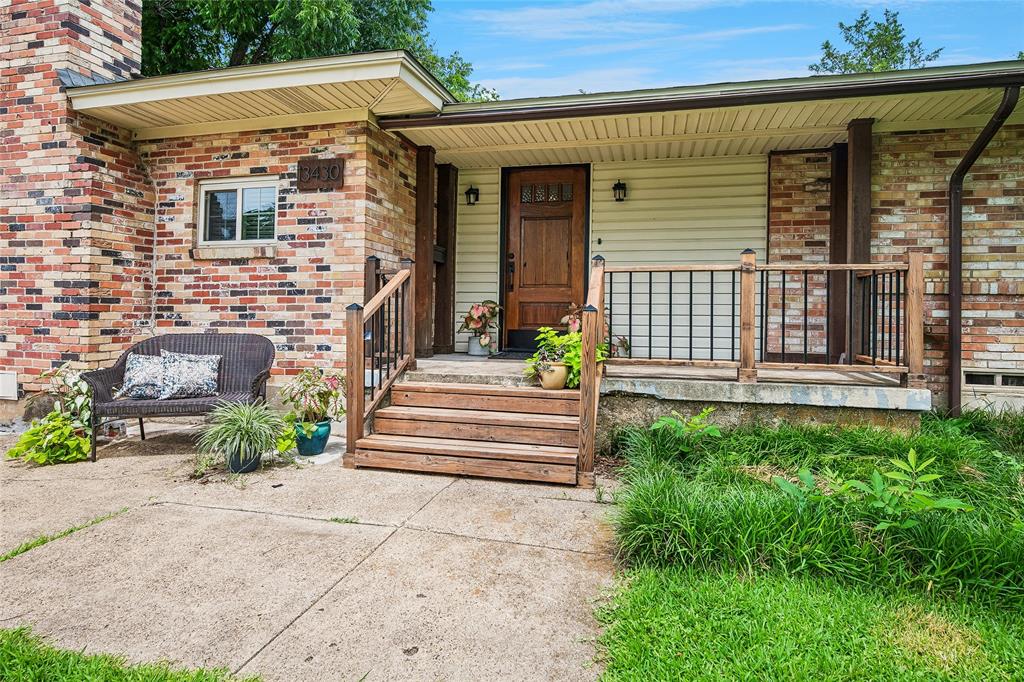 Inviting front porch accented with stained hardwood door. Brick and siding exterior featuring a covered porch with wood steps and railing, a solid wood entry door, and an exterior light fixture