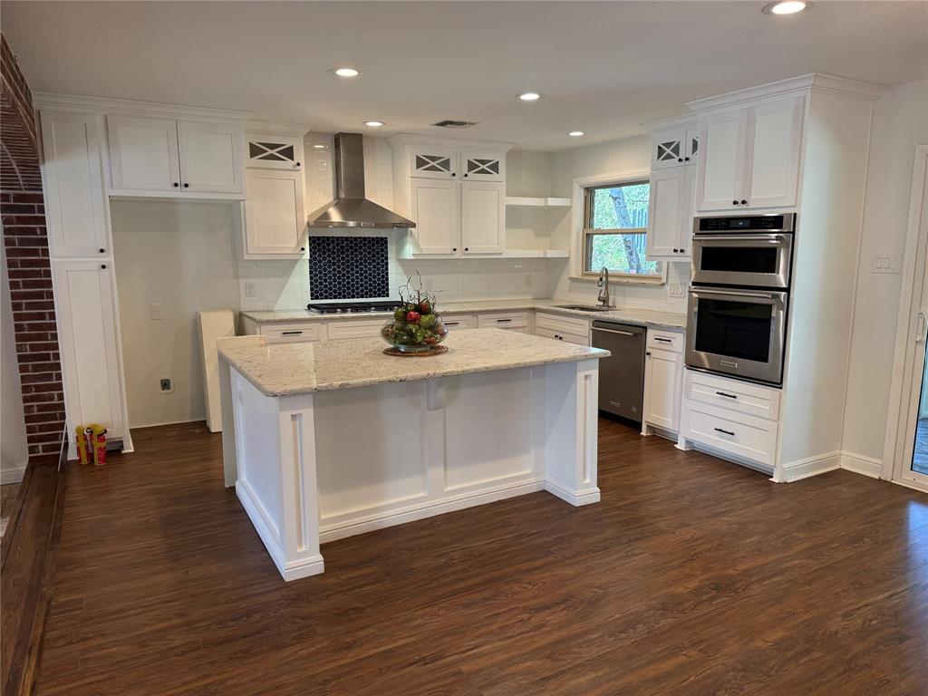 Spacious kitchen featuring an island with a light-toned countertop, white cabinetry with dark hardware, stainless steel appliances, and wood-finish flooring