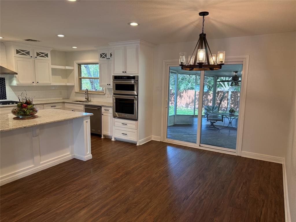 Kitchen featuring wood-finish flooring, white cabinetry, a granite island countertop, and built-in stainless steel appliances
