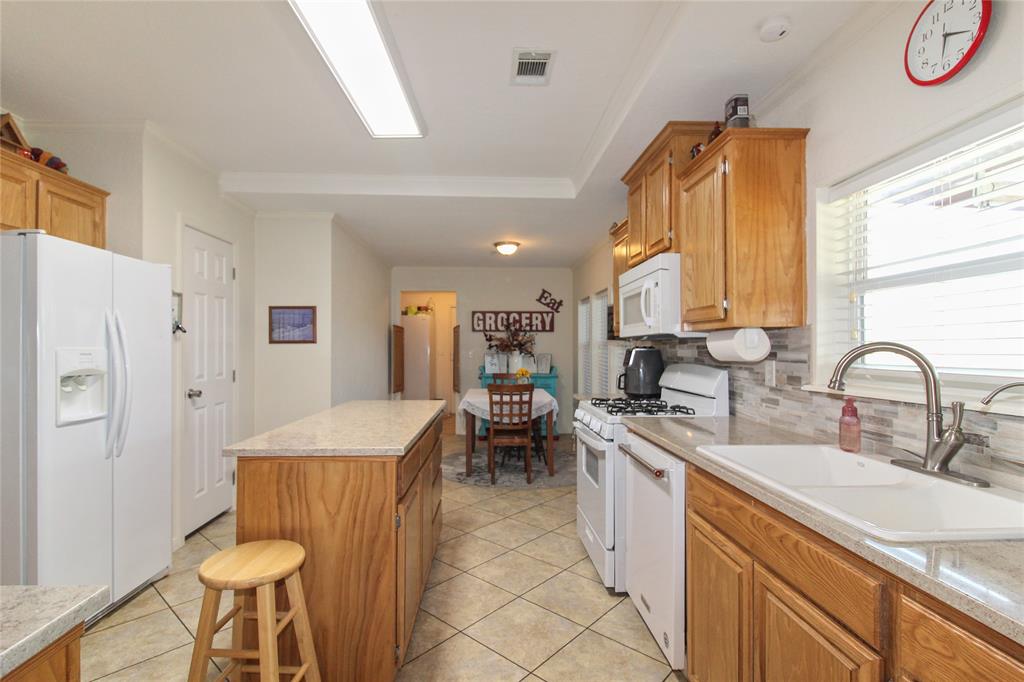Kitchen featuring wood cabinetry, light-toned countertops, a tile backsplash, and a large sink with a gooseneck faucet