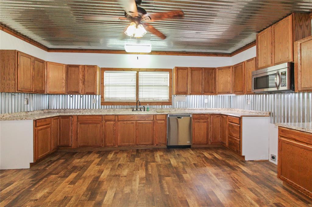 1936  HOUSE Kitchen featuring wood-finish flooring, extensive wood cabinetry, L-shaped countertops, stainless steel dishwasher, and a built-in microwave