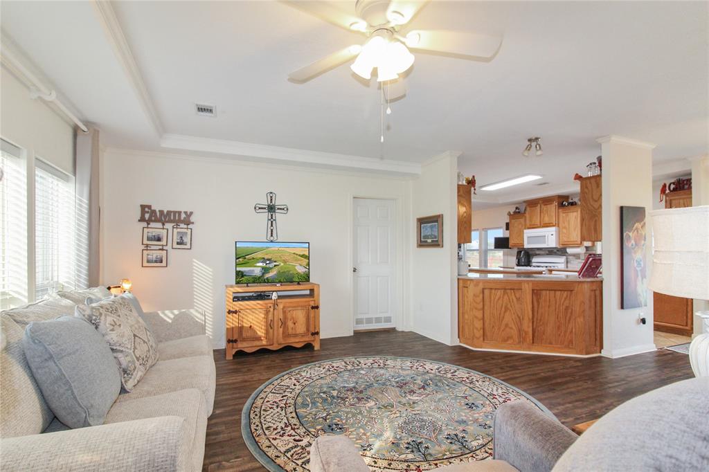Spacious living area featuring wood-finish flooring, ample natural light from multiple windows, and a ceiling fan